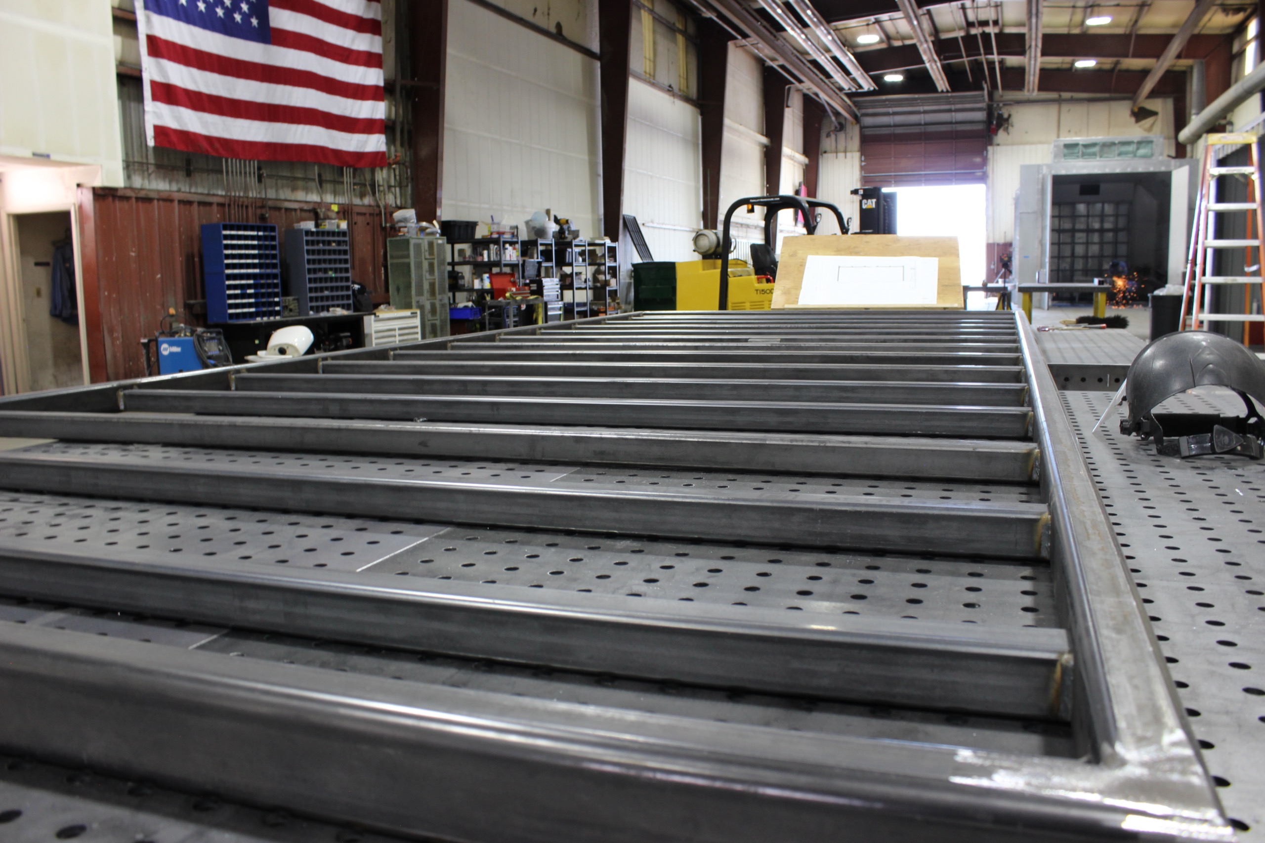Hero image of the Core-X Steel fabrication shop, welding project in the foreground and shop with American flag on the wall in the background.